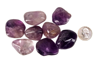 A pile of large amethyst tumbled stones with deep purple, to violet hues with a quarter for comparison. Most are larger than the quarter.