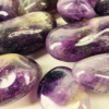 A closeup of amethyst tumbled medium, with violet hues, and some creamy white patterns in the stones with a good polish.
