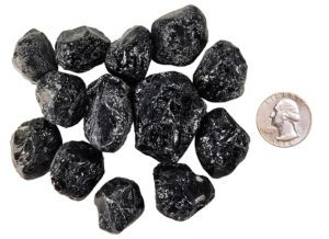 A pile of tumbled apache tears, showing deep black with some white patterns, and a quarter for comparison. Most are the same size or larger than the quarter.