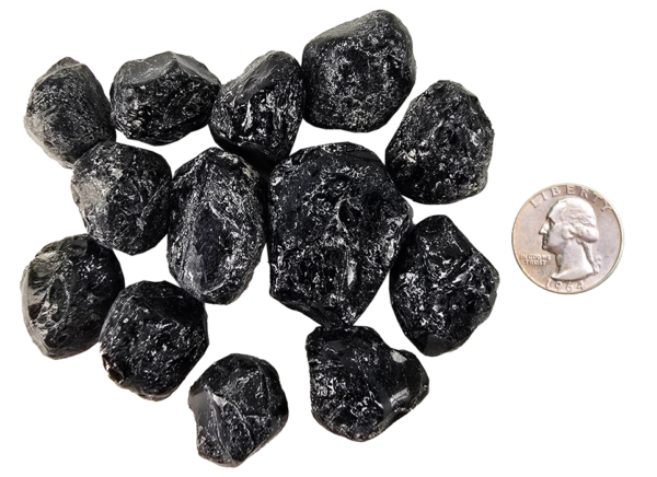 A pile of tumbled apache tears, showing deep black with some white patterns, and a quarter for comparison. Most are the same size or larger than the quarter.