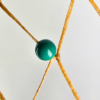 A closeup of a turquoise bead woven into a dream catcher.