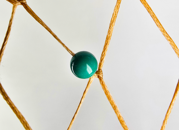 A closeup of a turquoise bead woven into a dream catcher.