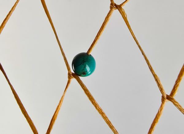 A closeup of a turquoise bead woven into a dream catcher.