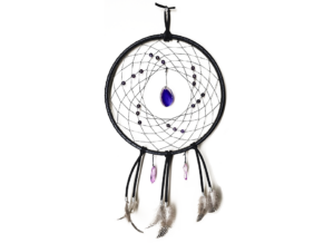 A black dream catcher showing a purple agate slice as the centerpiece, surrounded by amethyst beads woven into the dream catcher, and purple quarts crystals and feathers hanging bellow.