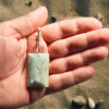 Aquamarine pendant with light blue, creamy yellowish white flowing through the polished stone, with a wire-wrapped silver bail being held in the palm of a hand with a desert background.