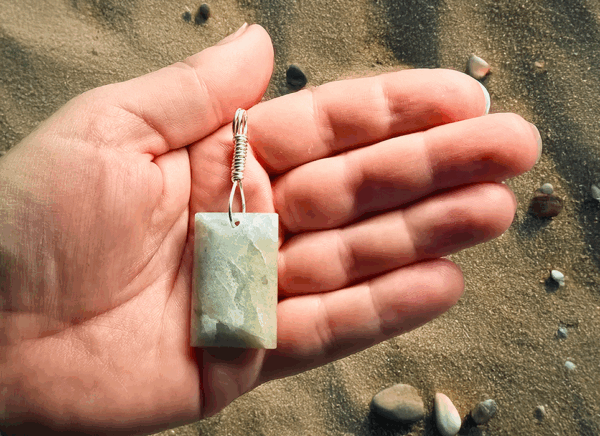 Aquamarine pendant with light blue, creamy yellowish white flowing through the polished stone, with a wire-wrapped silver bail being held in the palm of a hand with a desert background.