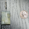 Aquamarine pendant with light blue, creamy yellowish white flowing through the polished stone, with a wire-wrapped silver bail. A quarter is displayed for size comparison, the pendant is almost double the diameter vertically, and slightly larger than it horizontally.