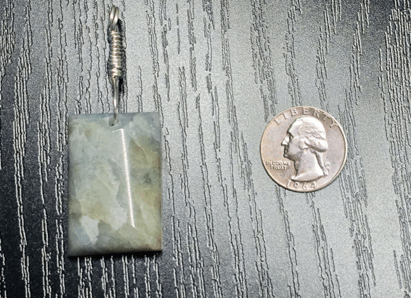 Aquamarine pendant with light blue, creamy yellowish white flowing through the polished stone, with a wire-wrapped silver bail. A quarter is displayed for size comparison, the pendant is almost double the diameter vertically, and slightly larger than it horizontally.