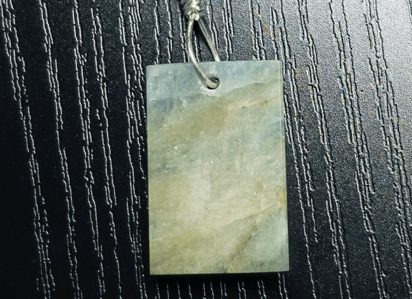 The back of aquamarine pendant with silver wire wrapped bail, showing more creamy yellowish white flowing through stone, and light blue.