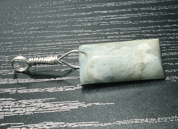 Aquamarine pendant sideways showing the shape of the cabochon, with light blue, creamy yellowish white flowing through the polished stone, with a wire-wrapped silver bail.