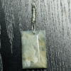 Closeup of Aquamarine pendant with light blue, creamy yellowish white flowing through the polished stone, with a wire-wrapped silver bail.