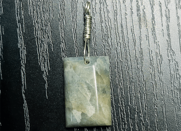 Closeup of Aquamarine pendant with light blue, creamy yellowish white flowing through the polished stone, with a wire-wrapped silver bail.