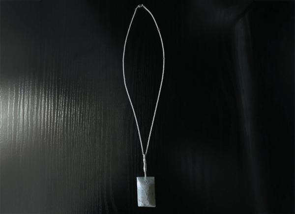 Aquamarine pendant with light blue, creamy yellowish white flowing through the polished stone, with a wire-wrapped silver bail displayed with a full silver necklace on a black table.