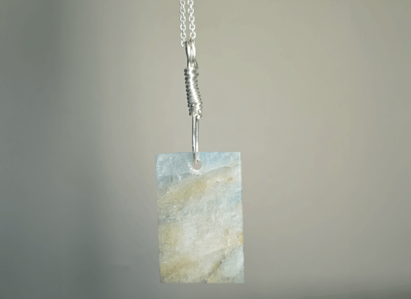 The back of aquamarine pendant with silver wire wrapped bail, showing more creamy yellowish white flowing through stone, and light blue.