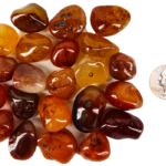 A pile of tumbled carnelian medium, with different shades of a brown honey color with some tranclucency to the polished stones, and a quarter for comparison. Most are slighlty smaller than the quarter.