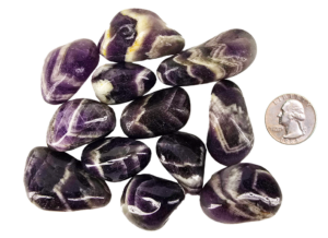 A pile of medium chevron amethyst polished stones, with deep purple to violet, with white in chevron patterns on the stones, and a quarter for comparison. Most are the same size or larger than the quarter.