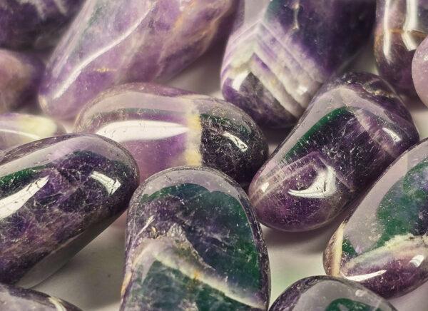 A closeup of small chevron amethyst polished stones, with deep purple to violet, with white in chevron patterns on the stones.