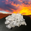 A pile of clear quartz crystals on display on a black table in the desert with a sunet in the background.