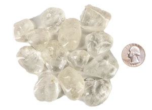 A pile of medium quartz tumbled stones, that are mostly transparent with some inclusions, with a quarter for comparison. Most are larger than the quarter, some the same size or slightly smaller.