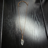 A quartz pendant with a copper wire wrapped bail with a wax cord adjustable necklace displayed on a black table.