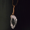 A quartz crystal pendant drilled that has a copper wire wrapped bail, with a black background showing the clarity of the crystal.