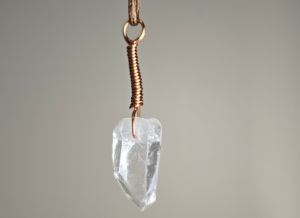 A quartz crystal pendant drilled that has a copper wire wrapped bail.