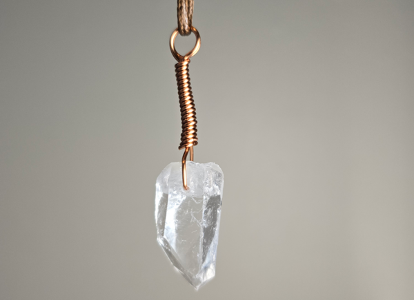 A quartz crystal pendant drilled that has a copper wire wrapped bail.