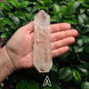 A large clear quartz point in the palm of a hand with a green, leafy background. It is quite large. Labeled 'A'.