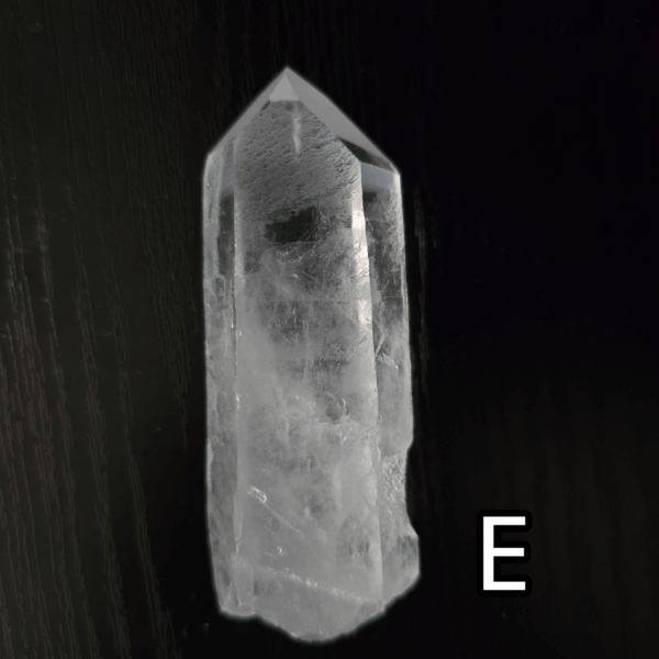 Large clear quartz crystal point with black backround, labeled 'E'.