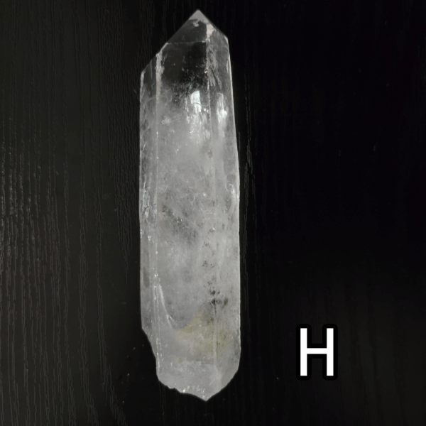 Large clear quartz crystal point with black backround, labeled 'H'.
