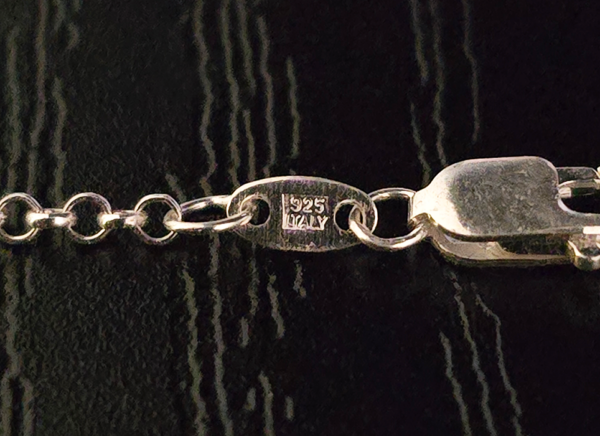 A closeup of the tag on the rolo adjustable sterling silver necklace, it is stamped '925 ITALY'.