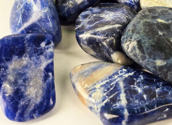 Closeup of medium sodalite tumbled group, showing deep blues and a range of milky to creamy white patterns.
