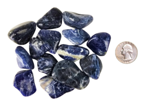 A pile of medium sodalite tumbled stones, showing deep blues and a range of milky to creamy white patterns with a quarter for comparison. Most are the size of the quarter and slightly larger.