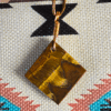 The back side of A yellow brown tiger's eye cabochon square shaped with a copper wire bail.