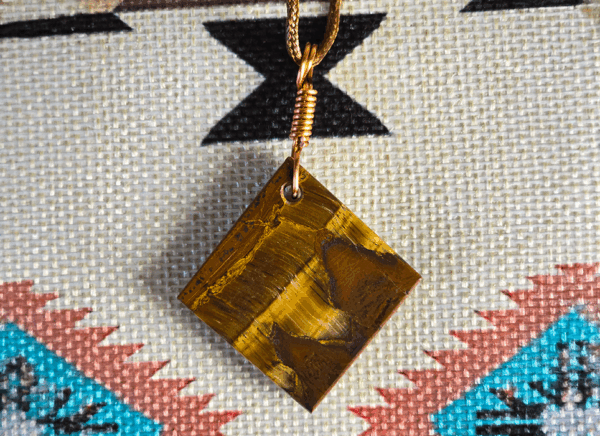 The back side of A yellow brown tiger's eye cabochon square shaped with a copper wire bail.