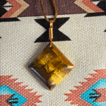 A yellow brown tiger's eye cabochon square shaped with a copper wire bail.