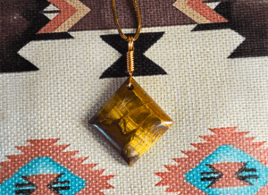 A yellow brown tiger's eye cabochon square shaped with a copper wire bail.