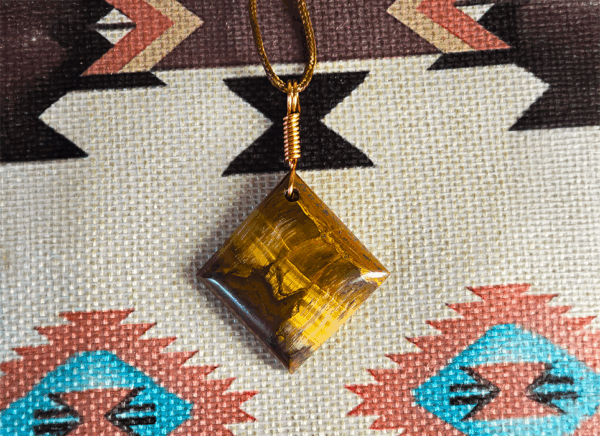 A yellow brown tiger's eye cabochon square shaped with a copper wire bail.