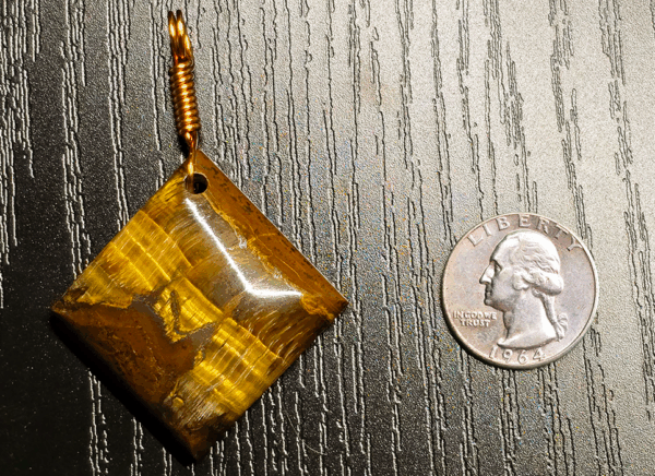 A yellow brown tiger's eye cabochon square shaped with a copper wire bail, and with a quarter for size comparison. It is a bit larger than the quarter.