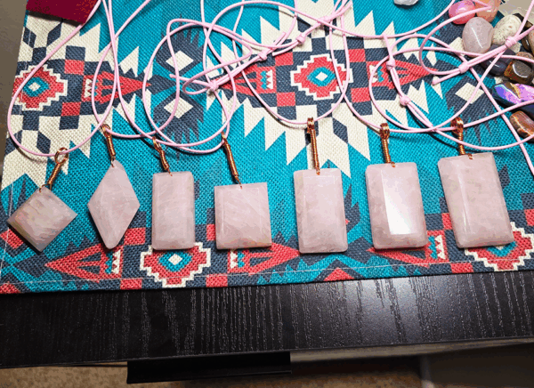 A group shot of faceted rose quartz pendants with wire wrapped bails on a southwest style decorative placemat.