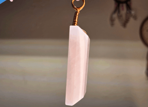 A pink rose quartz faceted pendant with a copper wire wrapped bail.