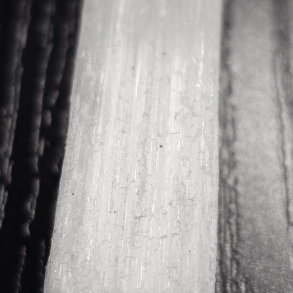 A closeup of a selenite stick, showing the fiber-like strands with a soft white glow.